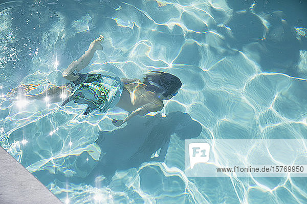 Junge schwimmt unter Wasser im sonnigen Sommerschwimmbad