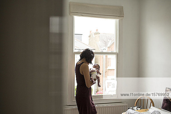 Mutter hält unschuldigen neugeborenen Jungen am Fenster