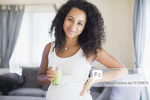 Portrait happy young pregnant woman drinking healthy green smoothie