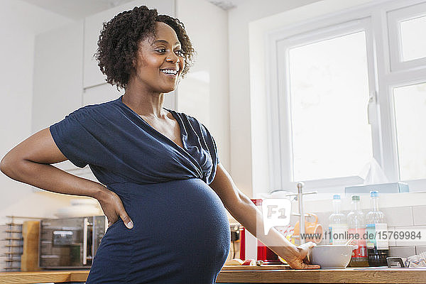 Glückliche schwangere Frau beim Essen in der Küche