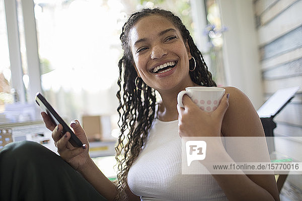 Portrait happy young woman with smart phone and tea laughing
