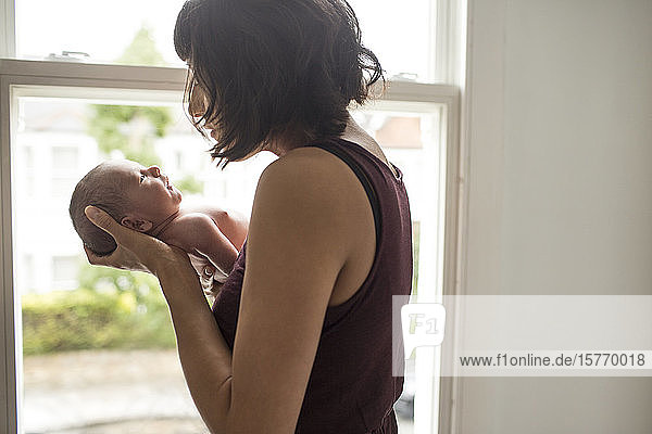 Mutter wiegt ihren neugeborenen Sohn am Fenster