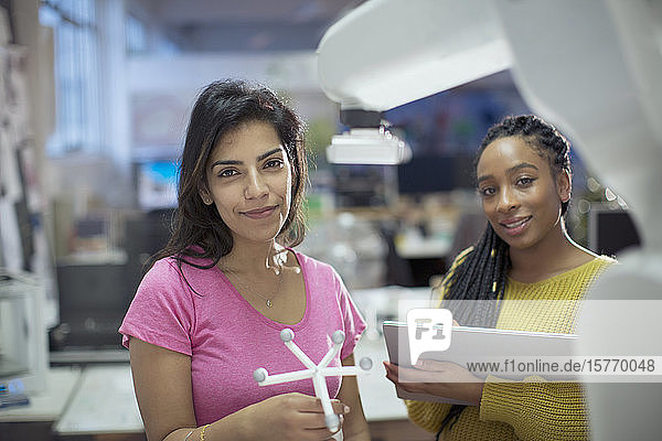 Portrait confident female engineers with prototype and robotic arm in office