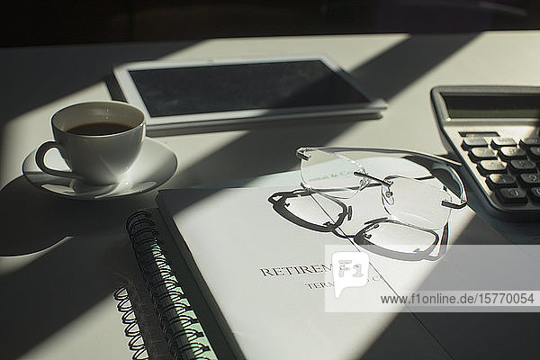 Ruhestandsportfolio auf sonnigem Schreibtisch mit Kaffee und Brille