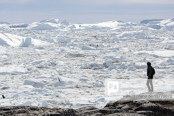 Mann auf Felsen mit Blick auf sonnige Gletscher Eisschmelze Blick Grönland