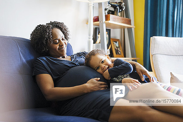 Porträt süßes Mädchen lehnt sich auf schwangere Mutter Bauch auf Sofa