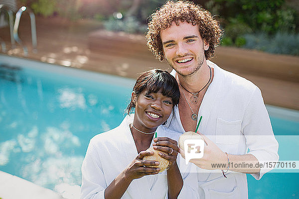 Porträt glückliches junges Paar in Bademänteln  das am Pool aus Kokosnüssen trinkt