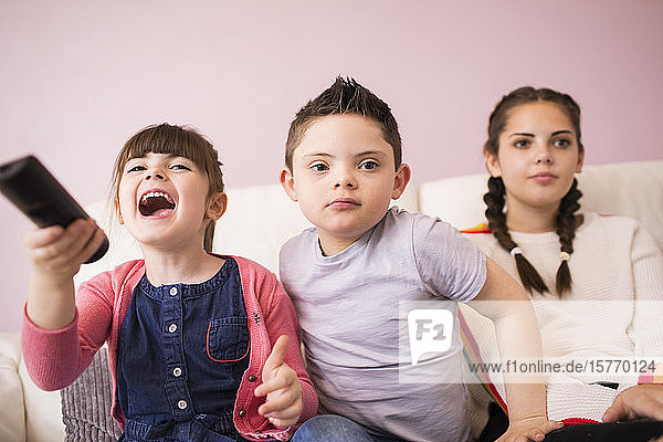 Sisters and brother with Down Syndrome watching TV on sofa