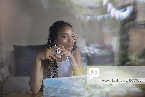 Nachdenkliche junge Frau trinkt Kaffee am Laptop im Fenster