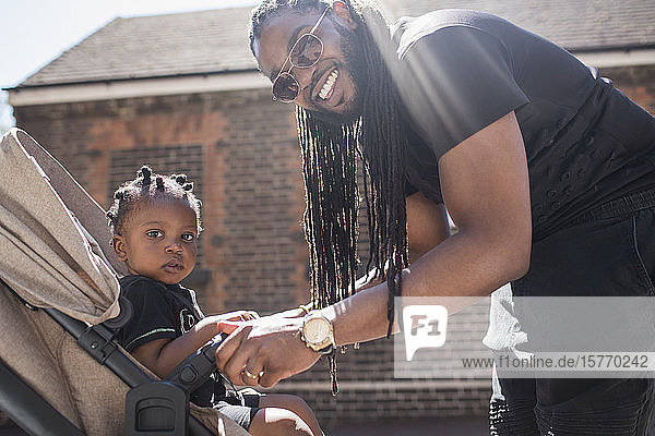 Porträt glücklicher Vater mit langen Zöpfen  der sein Kleinkind im Kinderwagen festhält