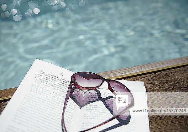 Heart-shape sunglasses on book at sunny poolside