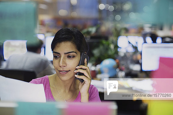 Geschäftsfrau  die mit einem Smartphone spricht und Papierkram im Büro liest