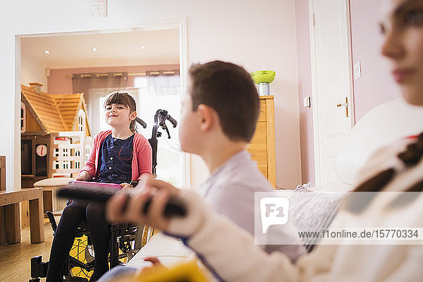 Happy girl in wheelchair with siblings at home