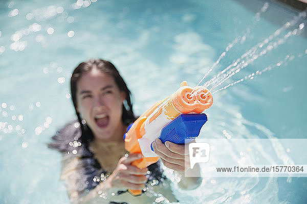 Playful woman using squirt gun in sunny summer swimming pool