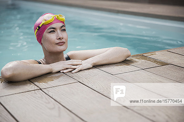 Selbstbewusste Frau mit Badekappe und Schwimmbrille lehnt sich an den Rand des Schwimmbeckens