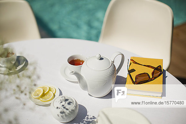 Teeservice und Buch auf dem sonnigen Tisch am Pool