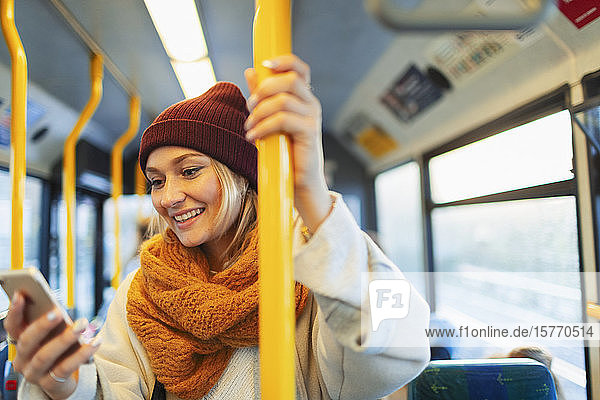 Junge Frau  die im Bus eine SMS mit ihrem Smartphone schreibt