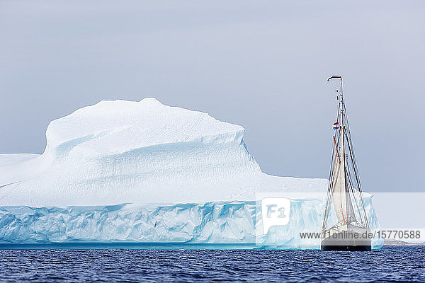 Schiff fährt entlang eines majestätischen Eisbergs auf dem Atlantischen Ozean in Grönland