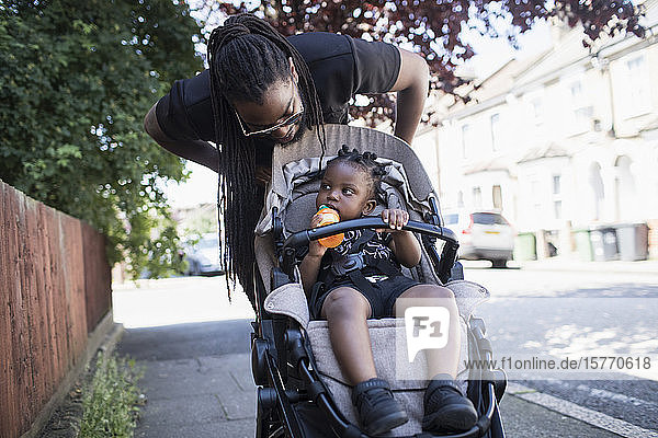 Vater schiebt sein Kleinkind im Kinderwagen auf dem Bürgersteig