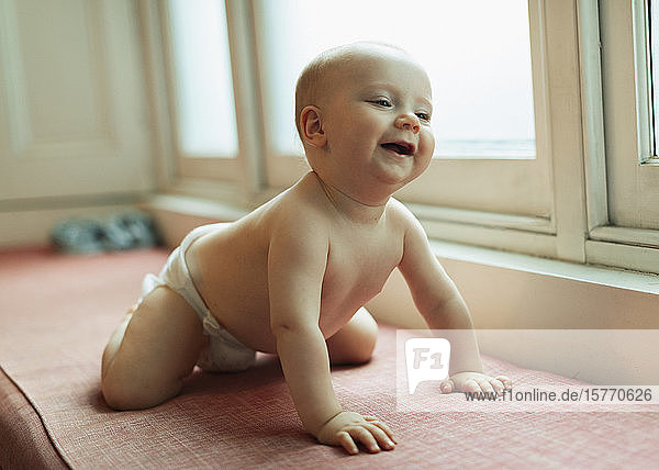 Niedliches Baby in Windel lachend auf Fensterbank