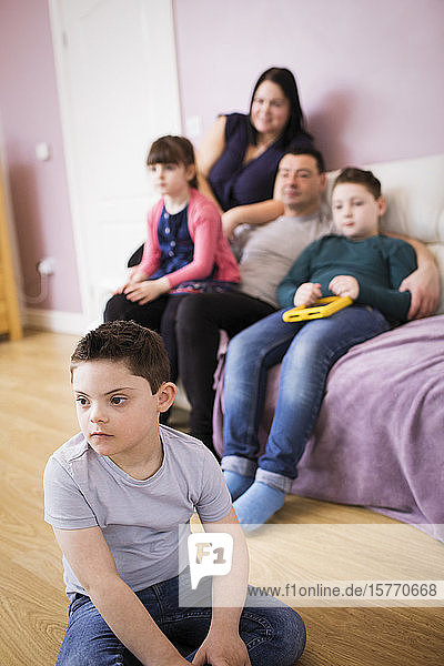 Junge mit Down-Syndrom sieht mit seiner Familie im Wohnzimmer fern