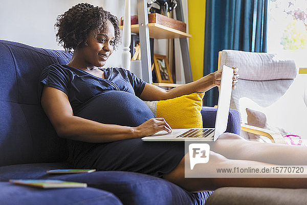 Schwangere Frau mit Laptop auf dem Sofa