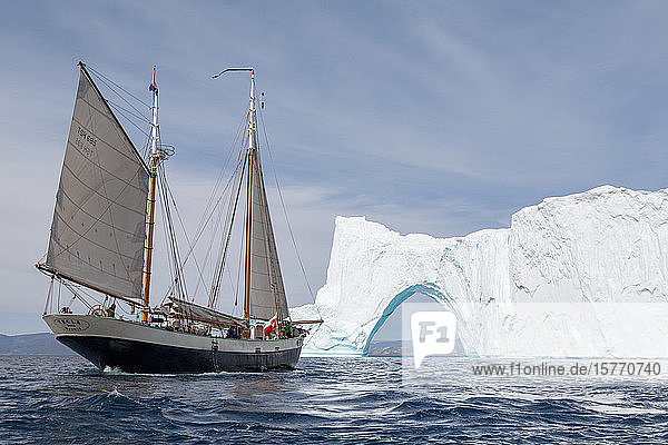 Schiff fährt durch Eisberg Bogen auf sonnigen blauen Atlantik Grönland