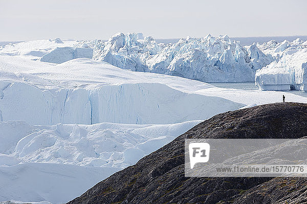 Man on cliff overlooking majestic polar glaciers Greenland