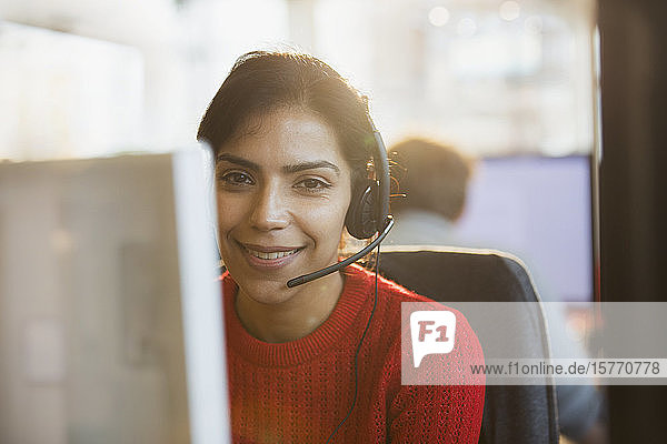 Porträt einer lächelnden  selbstbewussten Geschäftsfrau mit Headset bei der Arbeit am Computer im Büro