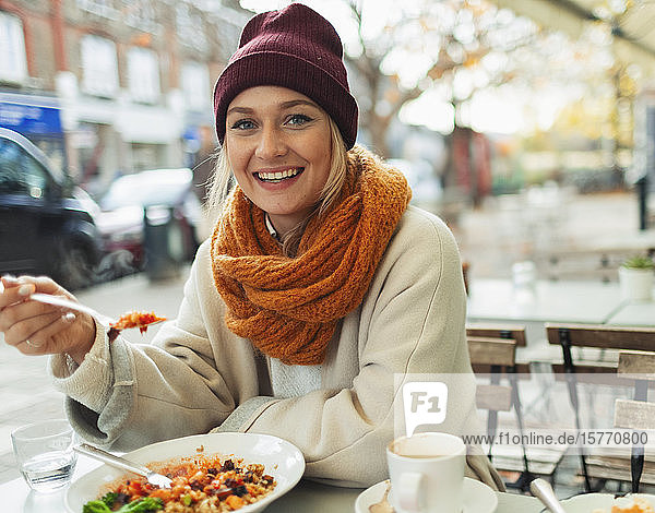 Porträt einer lächelnden Frau,  die im Herbst in einem Straßencafé zu Mittag isst