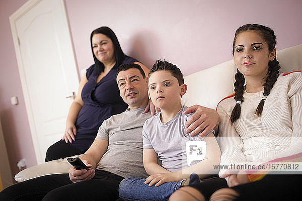 Familie mit Sohn mit Down-Syndrom sieht auf dem Wohnzimmersofa fern