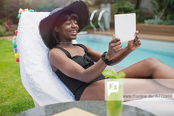 Glückliche junge Frau beim Videochat mit digitalem Tablet am Pool
