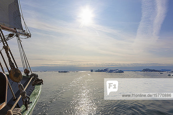 Segelboot auf dem sonnigen Atlantik mit schmelzenden Eisbergen in Grönland