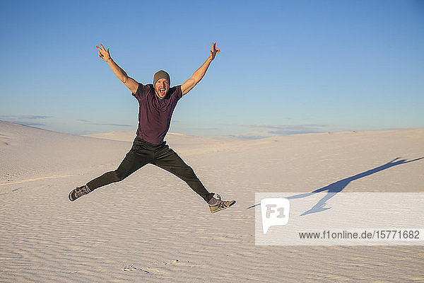 Unbeschwerter Mann in der Luft auf dem weißen Sand mit blauem Himmel  der einen Schatten neben ihn wirft  White Sands National Monument; Alamogordo  New Mexico  Vereinigte Staaten von Amerika