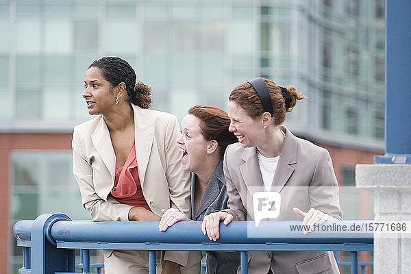 Drei Frauen stehen am Geländer und lachen.