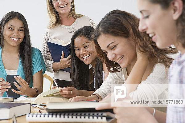 Vier Mädchen im Teenageralter lernen mit einem Lehrer  der neben ihnen steht