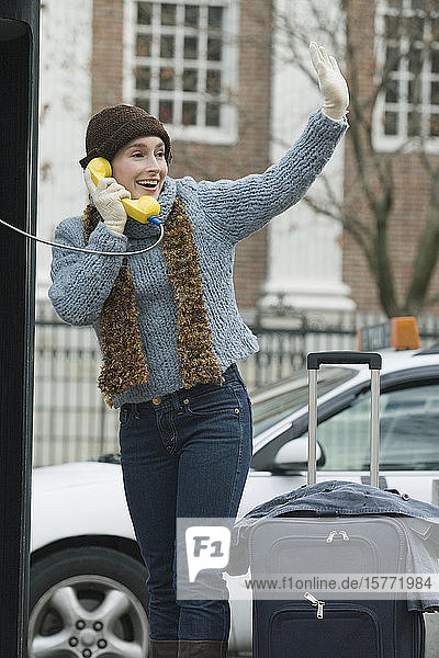 Young woman talking on a pay phone and waving her hand