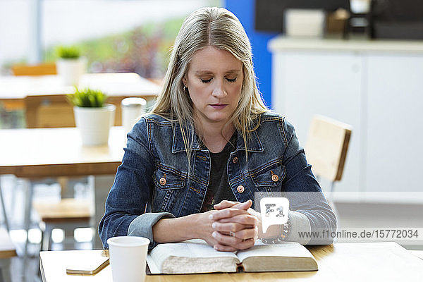 A mature woman praying  after doing some personal Bible study  in a coffee shop; Edmonton  Alberta  Canada