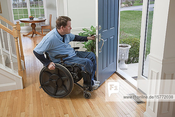 Ein Mann im Rollstuhl öffnet die Eingangstür seines Hauses und schaut hinaus