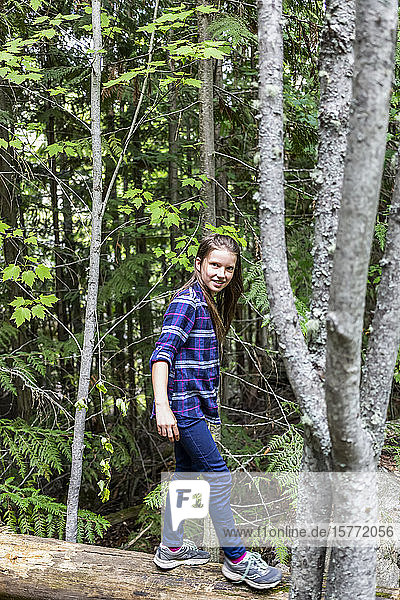 A pre-teen girl balances while walking on a log in a forest; Salmon Arm  British Columbia  Canada