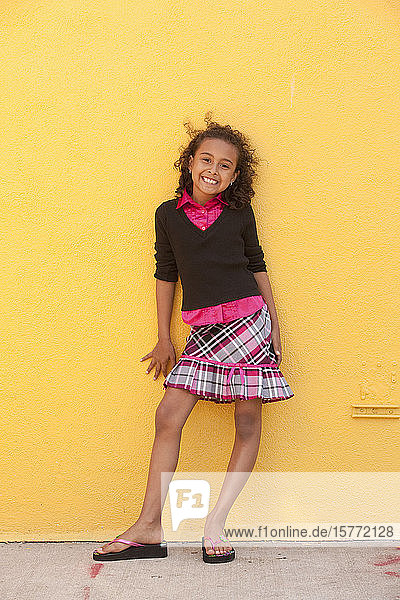 Porträt eines jungen hispanischen Mädchens  das vor einer leuchtend gelben Wand steht