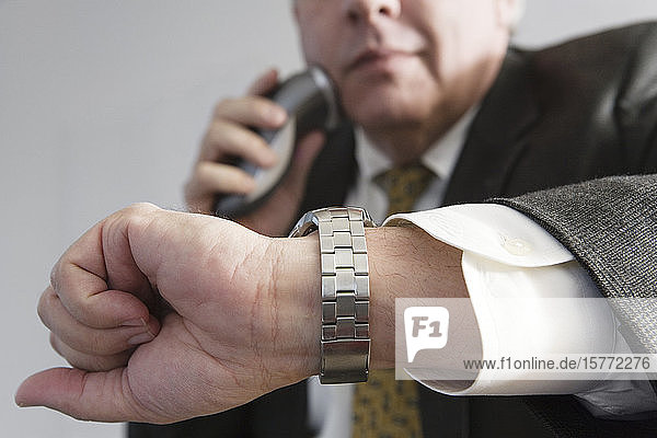 Blick auf einen Geschäftsmann  der die Zeit kontrolliert und einen elektronischen Rasierer bei der Arbeit benutzt.
