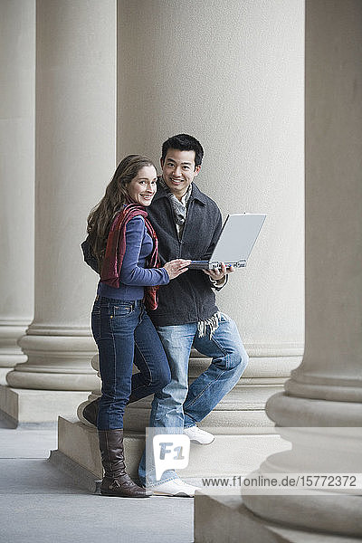 Porträt eines jungen Mannes  der einen Laptop hält und mit einer jungen Frau steht