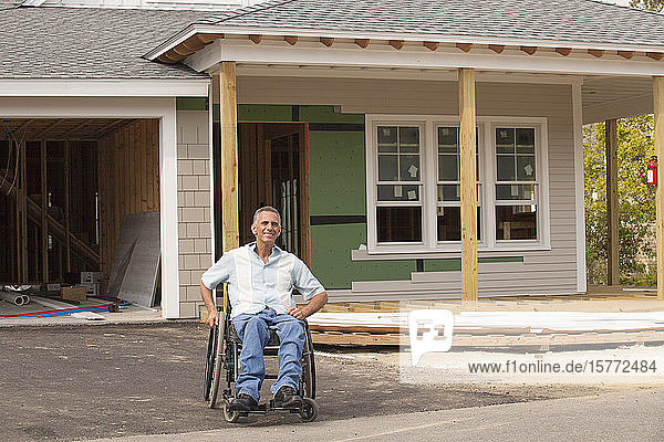 Mann im Rollstuhl vor einem neu gebauten Haus lächelt in die Kamera