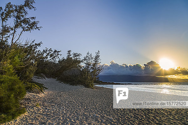 Ein schöner  warmer Sonnenuntergang an einem leeren Strand in Süd-Maui  Hawaii  wo nur ein paar Touristen den Sonnenuntergang in der Ferne beobachten. Dieser große weiße Sandstrand ist abgelegen und von Wald umgeben  ein echter hawaiianischer Rückzugsort für ruhige Touristen und Öko-Touristen; Maui  Hawaii  Vereinigte Staaten von Amerika