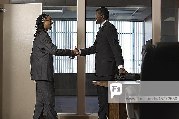 View of businessmen shaking hands in an office.