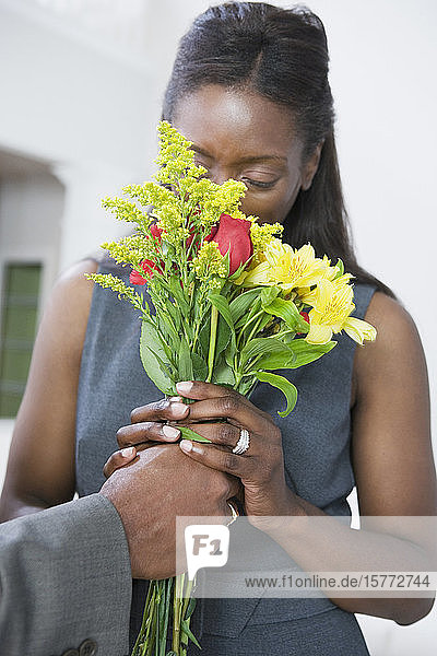 Frau mittleren Alters riecht an einem von einem Mann gehaltenen Blumenstrauß