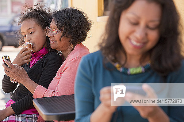 Junge Frau mit ihrem Smartphone  während ihre Mutter und ihre Tochter hinter ihr sitzen