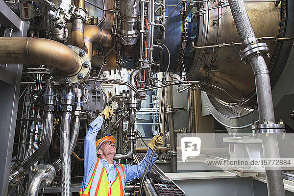Engineer examining instrumentation cables at fuel injection stage of gas turbine which drives generators in power plant while turbine is powered down