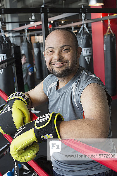 Young man with Down Syndrome wearing boxing gloves in a gym and smiling for the camera